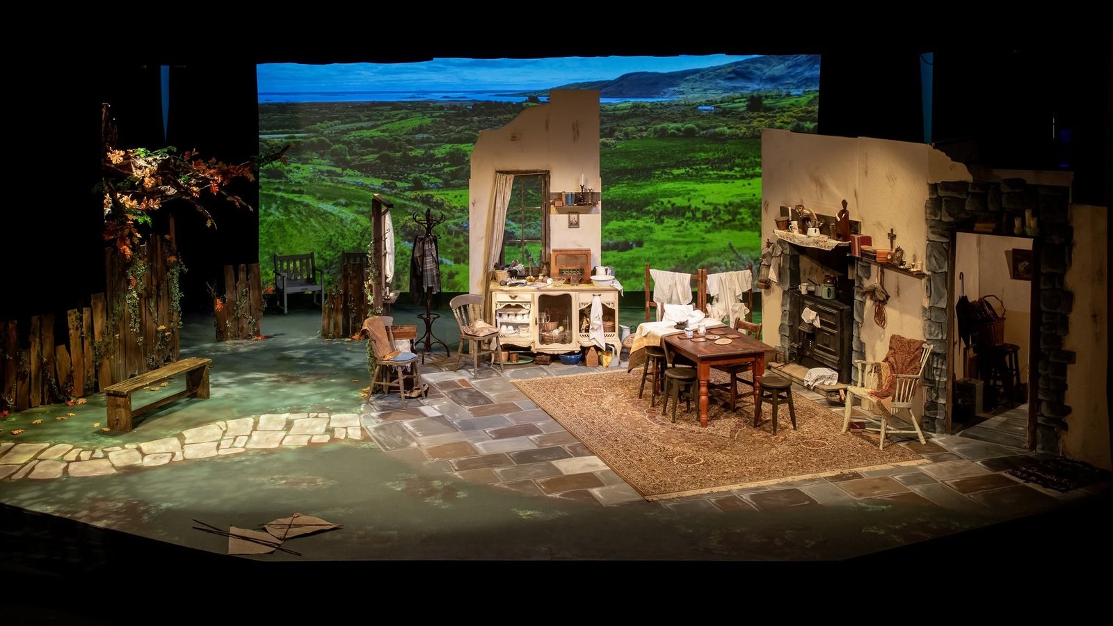 The stage set for Dancing at Lughnasa: a farmhouse kitchen with a dresser, table and range, open to a green Donegal hillside beyond