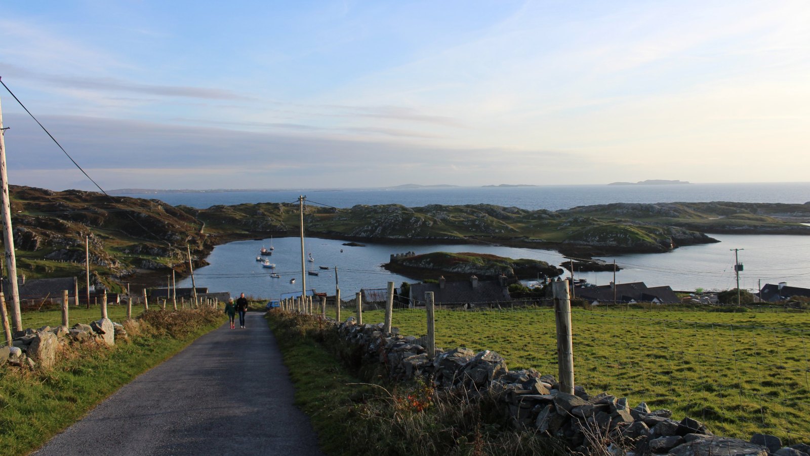 Boats at anchor in a sheltered harbour on Inishbofin, Co. Galway, seen from a quiet road above with the Atlantic beyond